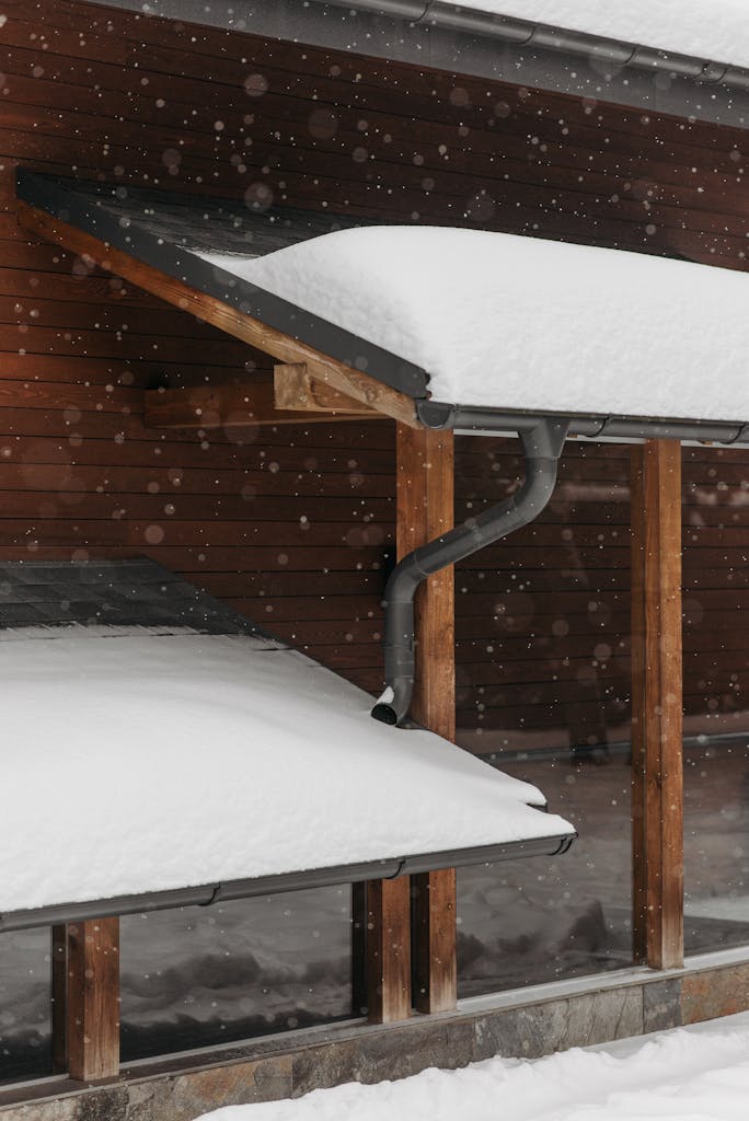 Snow-covered roofs with wooden structure during winter snowfall, capturing seasonal beauty.
