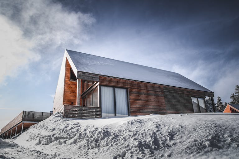 A contemporary wooden cabin with a snow-covered roof in a serene winter setting.