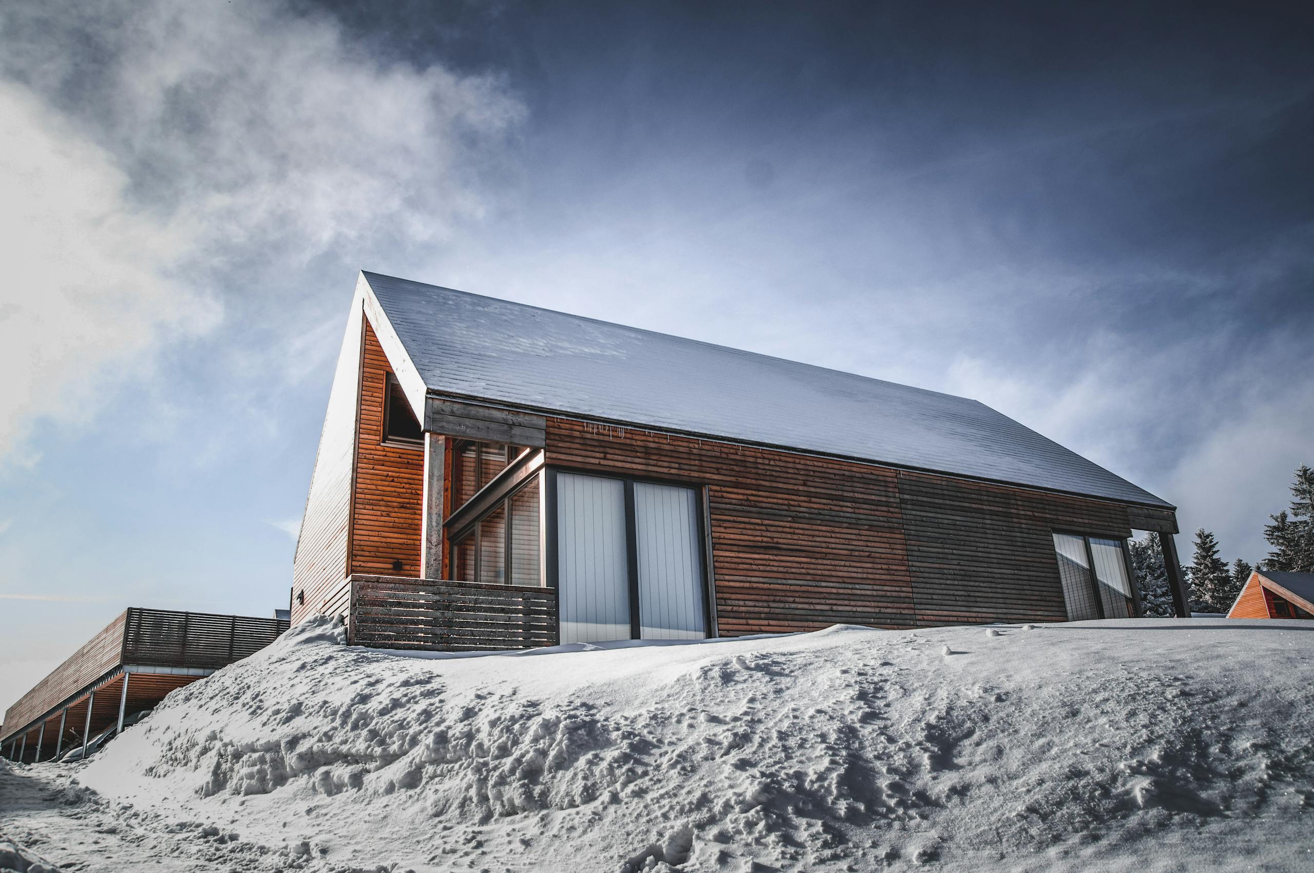 A contemporary wooden cabin with a snow-covered roof in a serene winter setting.