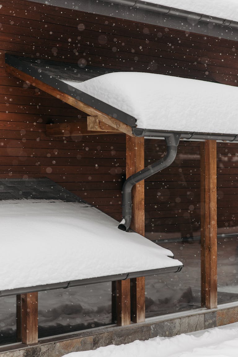 Snow-covered roofs with wooden structure during winter snowfall, capturing seasonal beauty.