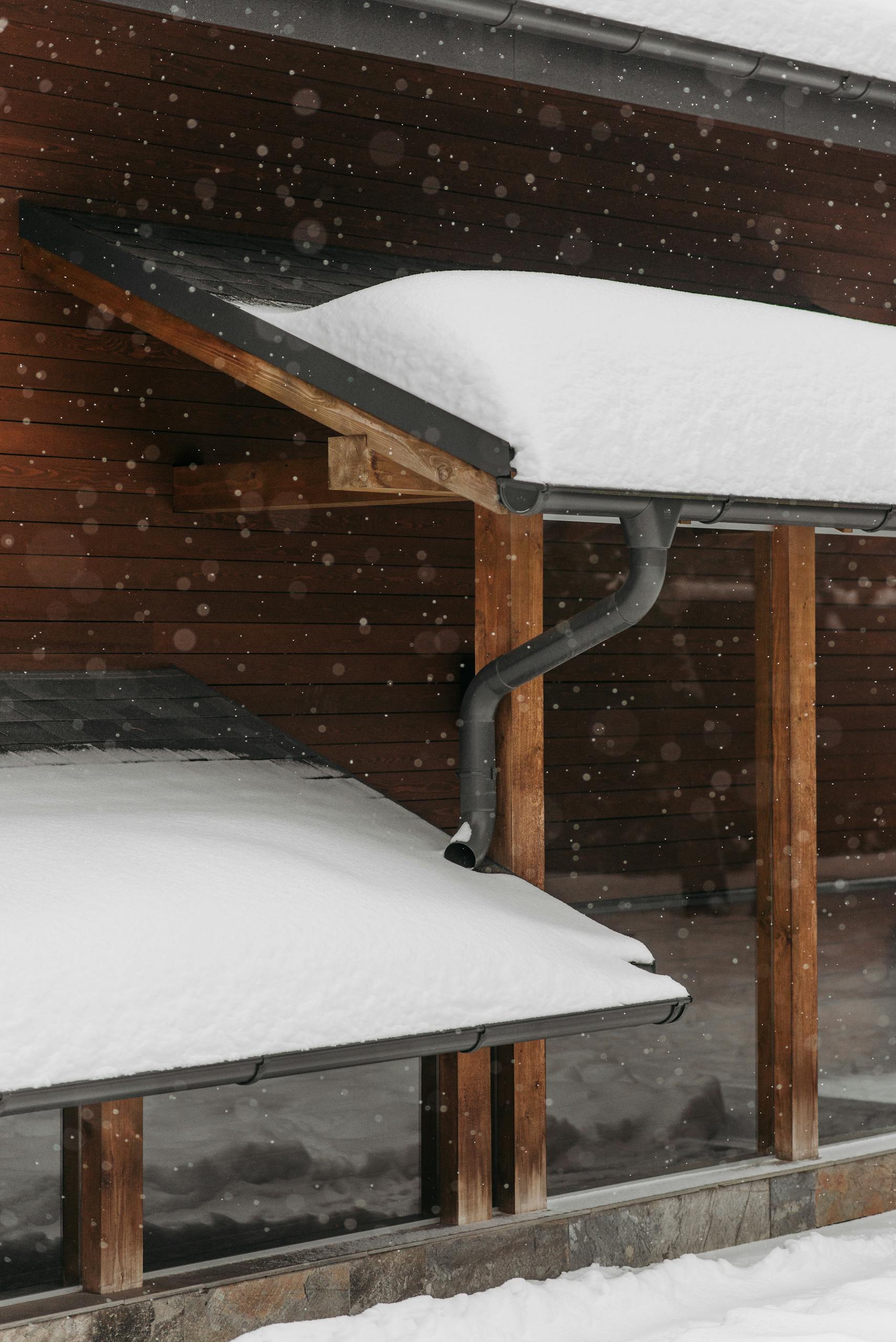 Snow-covered roofs with wooden structure during winter snowfall, capturing seasonal beauty.